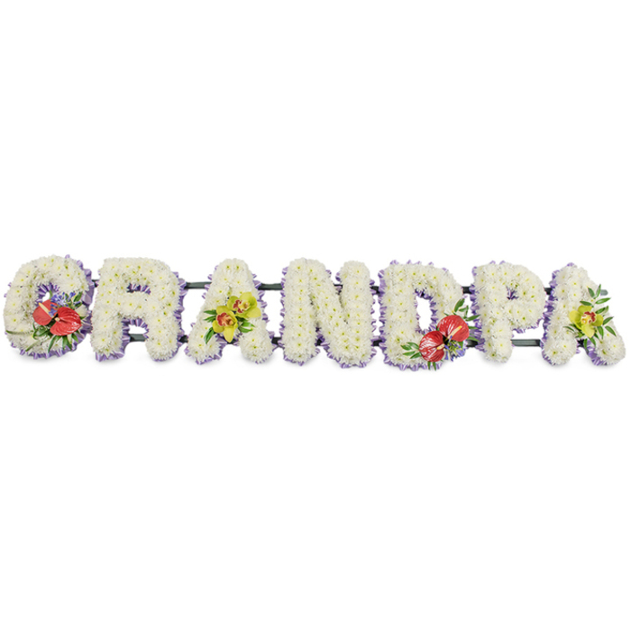 This photograph presents a beautifully arranged floral tribute spelling the word "GRANDPA" in bold, upright capital letters, placed against a pure white background that draws attention to every petal and detail. Each letter is meticulously crafted from clusters of small white chrysanthemums, tightly packed so that their soft, rounded petals create a dense, cushion-like finish, reminiscent of a gentle, white blanket laid in honour of a cherished grandfather. Along the base of each letter runs a narrow band of pale lavender ribbon, only slightly visible beneath the blooms, providing a subtle but effective outline that enhances the clarity and elegance of the word. The entire tribute is supported by dark green bars that run horizontally behind the letters, sturdy yet visually unobtrusive, making the design suitable for display at a funeral in Herne Hill or at a graveside ceremony nearby. Carefully chosen accent flowers are arranged to bring depth and warmth. The "G" and "D" feature striking groups of deep red anthuriums, their glossy, heart-shaped spathes and central spadices rising from rich green foliage and delicate purple fillers, introducing a bold note of love and remembrance. The first and last "A" are accented with refined yellow-green orchids, their graceful petals and slightly arching stems adding softness and a hint of hope. The white chrysanthemums convey serenity, while the red and green accents suggest the richness of family bonds. It's easy to imagine this bespoke "Grandpa" tribute resting near Brockwell Park Chapel or being carried gently into a small Herne Hill church, chosen by family members who want a floral memorial that feels personal, respectful, and lovingly made.