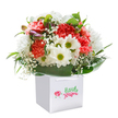 Bursting with personality and freshness, this joyful bouquet sits proudly within a neat white gift bag, its presentation reminiscent of a thoughtful gesture exchanged on a sunny stroll through Herne Hill Village. The soft coral, peach, and ruby carnations-each petal luxuriously ruffled-mingle with bright white daisies crowned in green-gold, sending sparks of happiness like laughter echoing through Brockwell Park's open fields. Baby's breath dances through the bouquet, airy and delicate, while unopened buds tinged with purple peek from the left as if shyly joining the celebration. A band of shining, deep green leaves unfolds around the flowers, cradling the whole in loving support. Perfectly rounded and balanced, the arrangement glows against a white background, its mood optimistic and open-hearted-ideal for birthdays, congratulations, or just to brighten a home across Herne Hill and Dulwich. Every bloom and touch of foliage whispers of local passion, skill, and the shared joy that flowers always seem to bring.